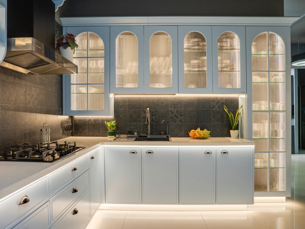 Luxury modern modular kitchen designed by Quodex in Mumbai, featuring light blue shaker-style cabinets, elegant arched fluted-glass overhead units with warm LED ambient lighting, a dark patterned tile backsplash, white quartz countertops, and seamlessly integrated built-in appliances.