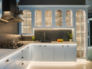 Luxury modern modular kitchen designed by Quodex in Mumbai, featuring light blue shaker-style cabinets, elegant arched fluted-glass overhead units with warm LED ambient lighting, a dark patterned tile backsplash, white quartz countertops, and seamlessly integrated built-in appliances.