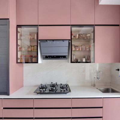 Modern straight modular kitchen with matte pink handleless cabinets, white quartz countertop, built-in chimney, three-burner gas hob, sink, and glass display cabinets.
