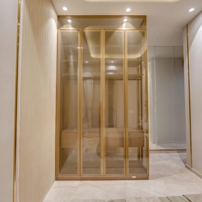 Luxury glass wardrobe with gold frame, tinted glass doors, and built-in storage in a modern bedroom