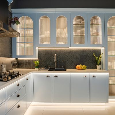 Luxury modern modular kitchen designed by Quodex in Mumbai, featuring light blue shaker-style cabinets, elegant arched fluted-glass overhead units with warm LED ambient lighting, a dark patterned tile backsplash, white quartz countertops, and seamlessly integrated built-in appliances.